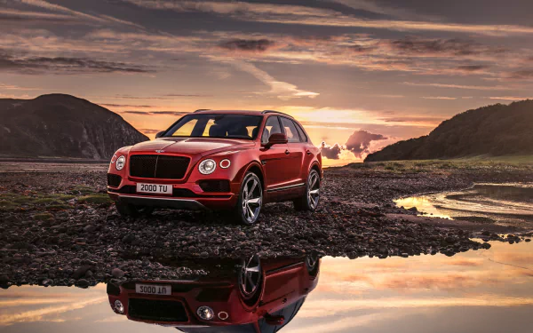 HD desktop wallpaper featuring a Bentley Bentayga car reflecting on a calm water surface, with a scenic background of mountains and a sunset sky.