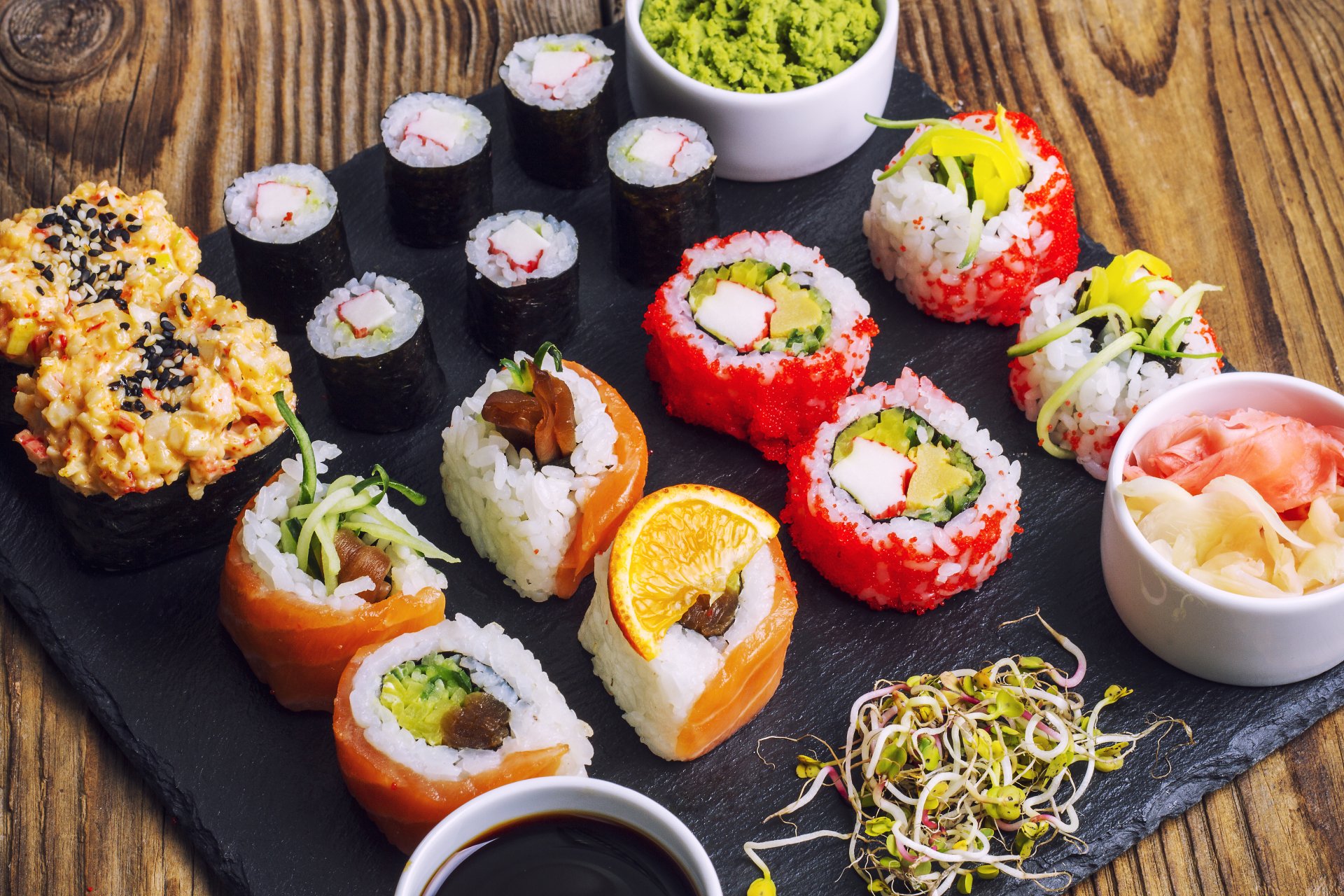 5K Ultra HD PC desktop wallpaper of assorted sushi food: seafood and fish rolls over rice, with wasabi, pickled ginger, soy sauce and sprouts on a slate board.