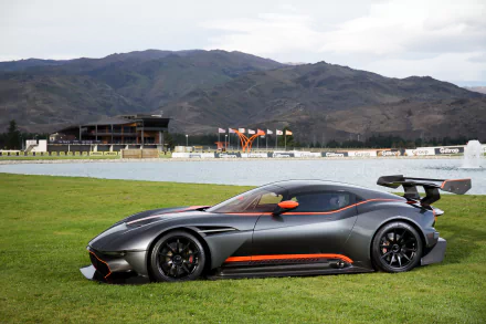 A sleek Aston Martin Vulcan supercar race car parked on grass with a mountainous background, captured in high-definition for a PC desktop wallpaper.