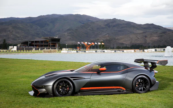 A sleek Aston Martin Vulcan supercar race car parked on grass with a mountainous background, captured in high-definition for a PC desktop wallpaper.