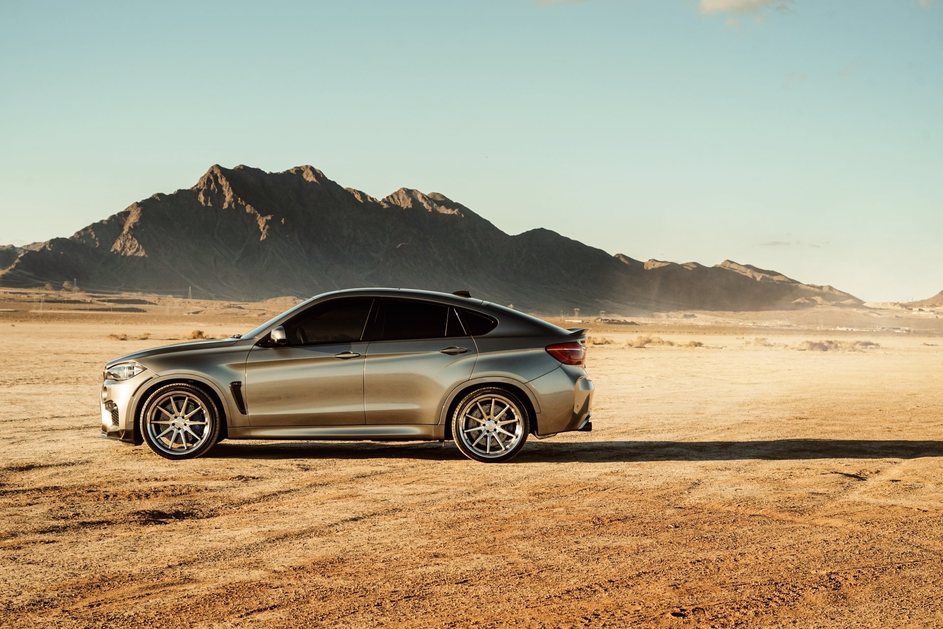 A silver BMW X6 SUV parked on a desert landscape with mountains in the background, captured in 4K Ultra HD for a PC desktop wallpaper.