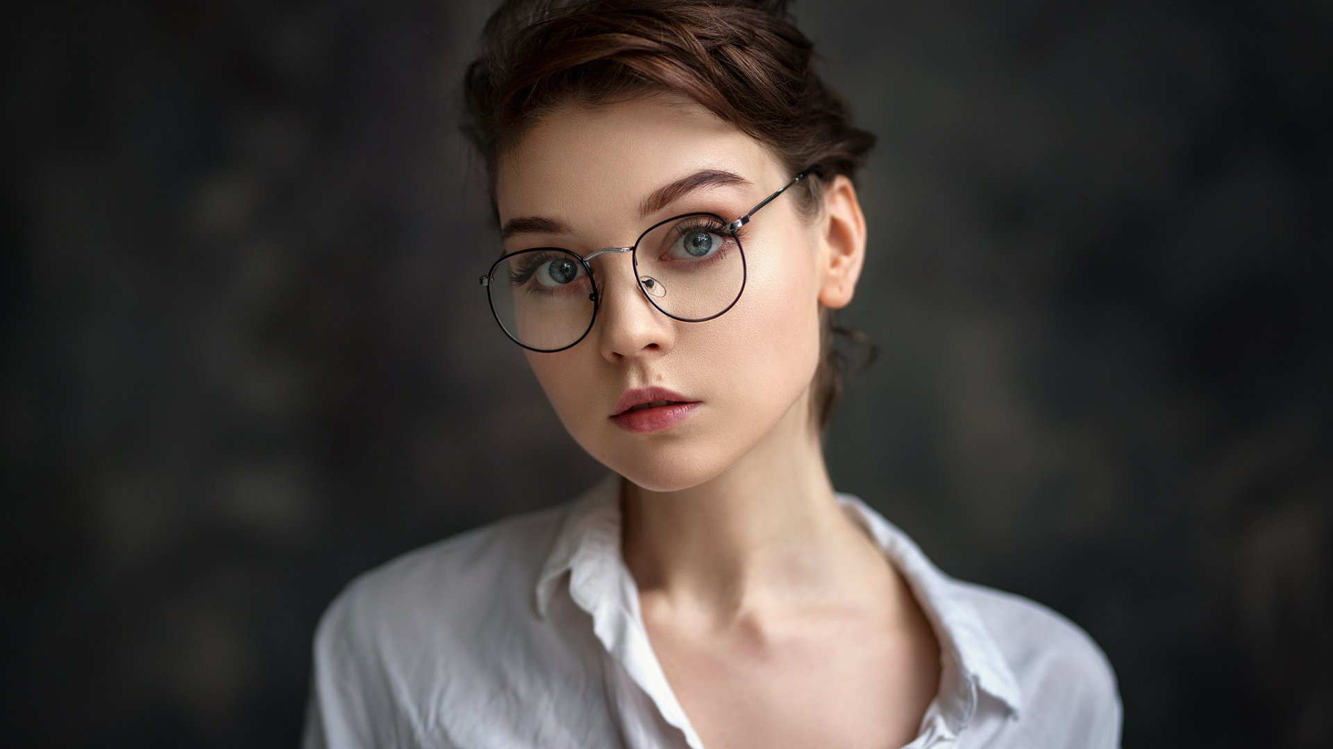 HD desktop wallpaper of a brunette model woman with blue eyes and glasses, featuring a close-up portrait of Olya Pushkina against a dark blurred background.