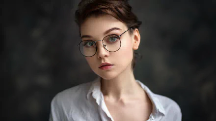 HD desktop wallpaper of a brunette model woman with blue eyes and glasses, featuring a close-up portrait of Olya Pushkina against a dark blurred background.