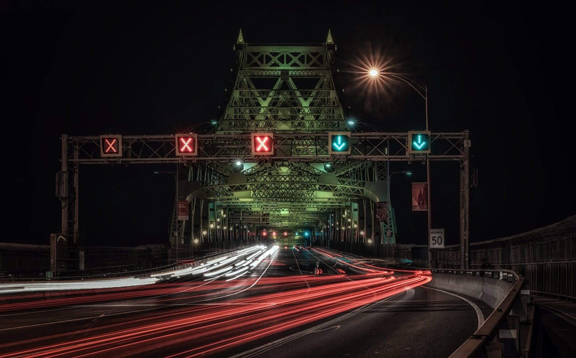Time-lapse photography of a bridge and road at night, capturing streaks of car lights under illuminated traffic signals in an HD desktop wallpaper.