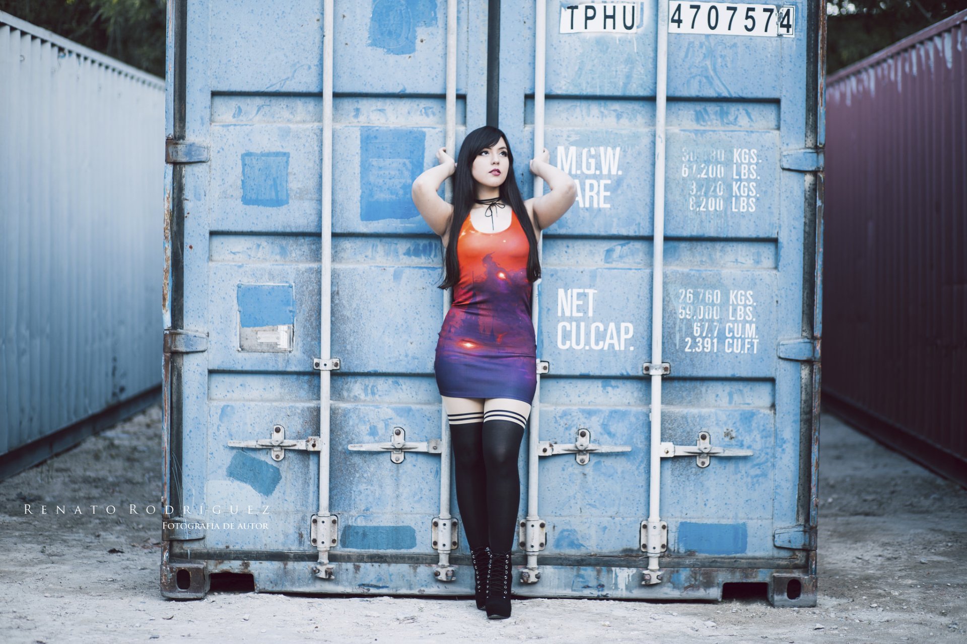 A cosplay model with black hair and brown eyes wearing lipstick, high heels, and a dress poses confidently against a blue shipping container in this HD Judy's Lullaby desktop wallpaper.