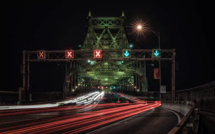 Time-lapse photography of a bridge and road at night, capturing streaks of car lights under illuminated traffic signals in an HD desktop wallpaper.