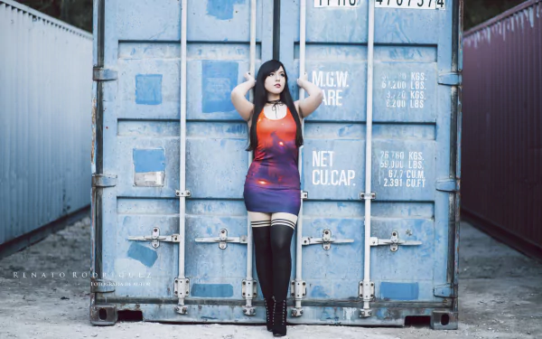 A cosplay model with black hair and brown eyes wearing lipstick, high heels, and a dress poses confidently against a blue shipping container in this HD Judy's Lullaby desktop wallpaper.