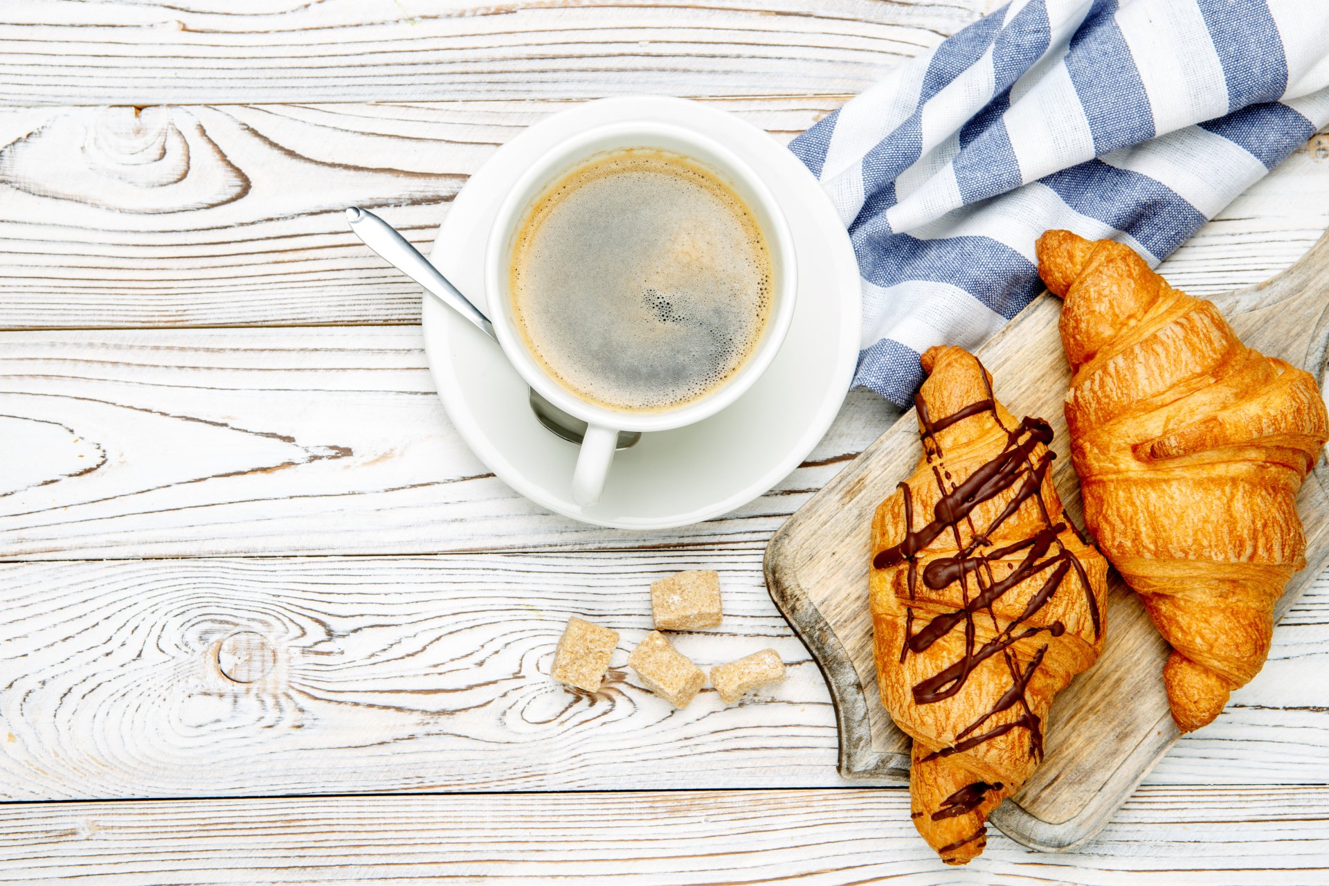 4K Ultra HD still life of a cup of coffee and two viennoiserie croissants on a wooden table with a striped cloth.