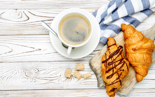 4K Ultra HD still life of a cup of coffee and two viennoiserie croissants on a wooden table with a striped cloth.