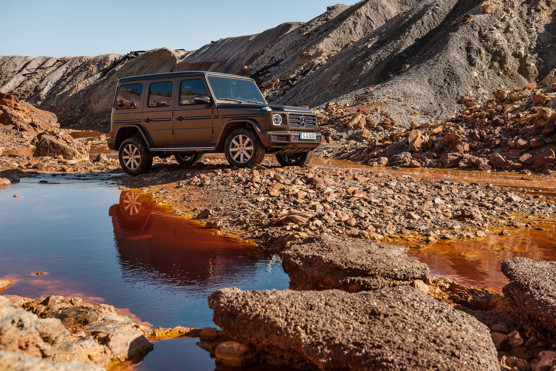 Silver Mercedes-Benz G-Class SUV parked on rocky terrain near a reflective water pool, captured in high-definition as a striking PC desktop wallpaper background.