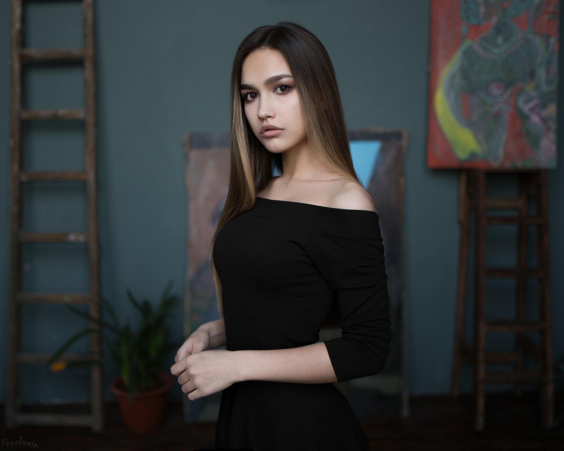 A woman with long brunette hair and brown eyes poses confidently in a black dress against a softly colored background, creating an elegant and striking HD wallpaper.