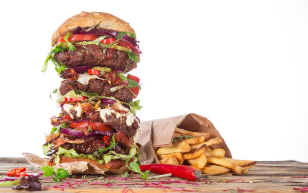 A 4K Ultra HD still life of a towering burger stacked with peppers, fresh greens, and sauces, accompanied by crispy French fries on a rustic wooden surface.