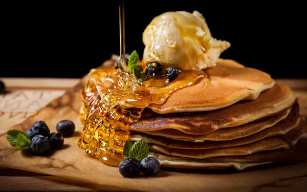 A stack of pancakes topped with honey drizzle, a scoop of ice cream, fresh blueberries, and mint leaves, captured in a vibrant HD still life food wallpaper.