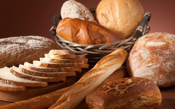 Food, bread: assorted rustic loaves, sliced bread, baguettes and rolls in a basket on a wooden surface — 4K Ultra HD PC desktop wallpaper and background.