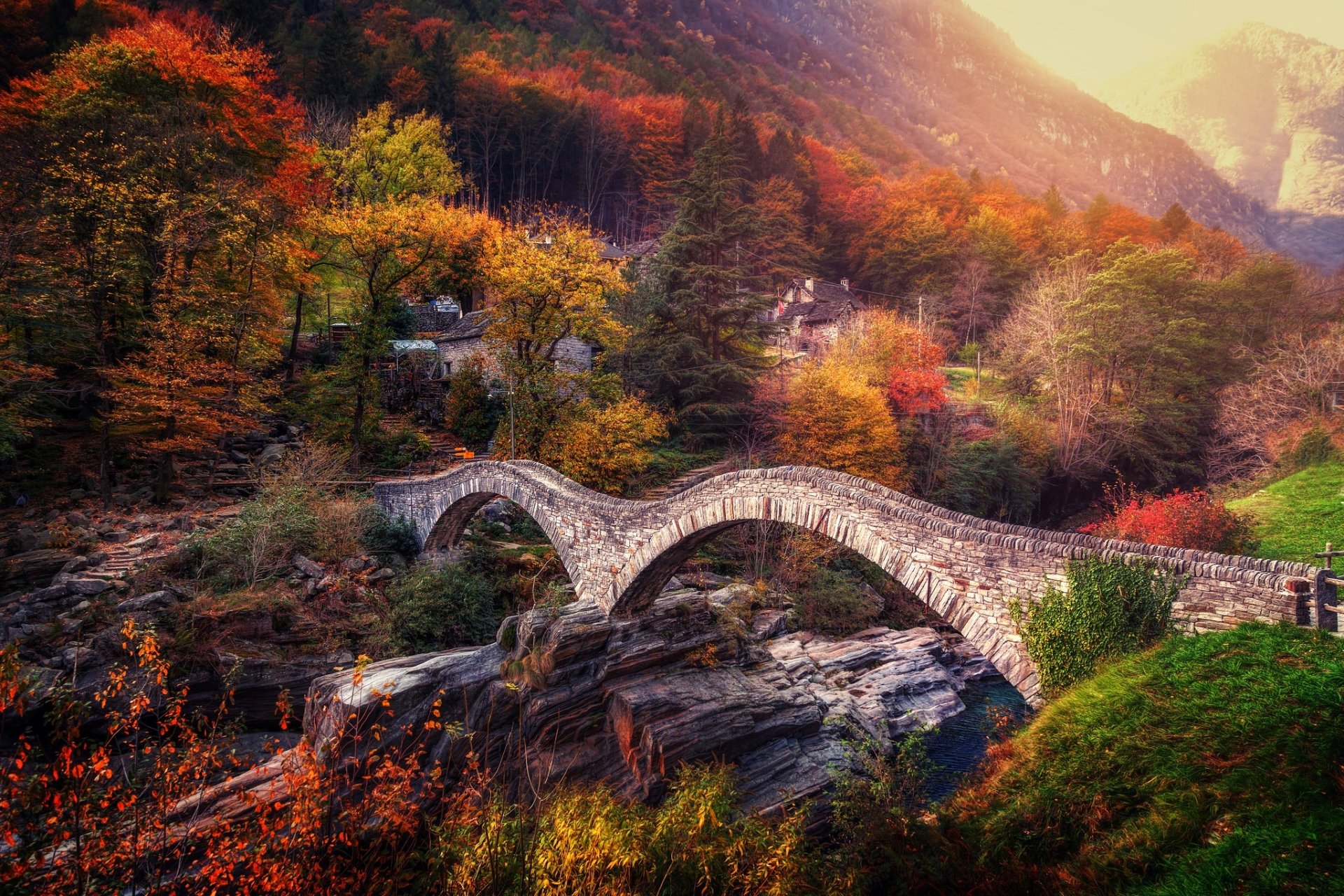 HD wallpaper of a stone bridge spanning a rocky creek in a vibrant fall forest, showcasing nature’s colors blending with man-made architecture.