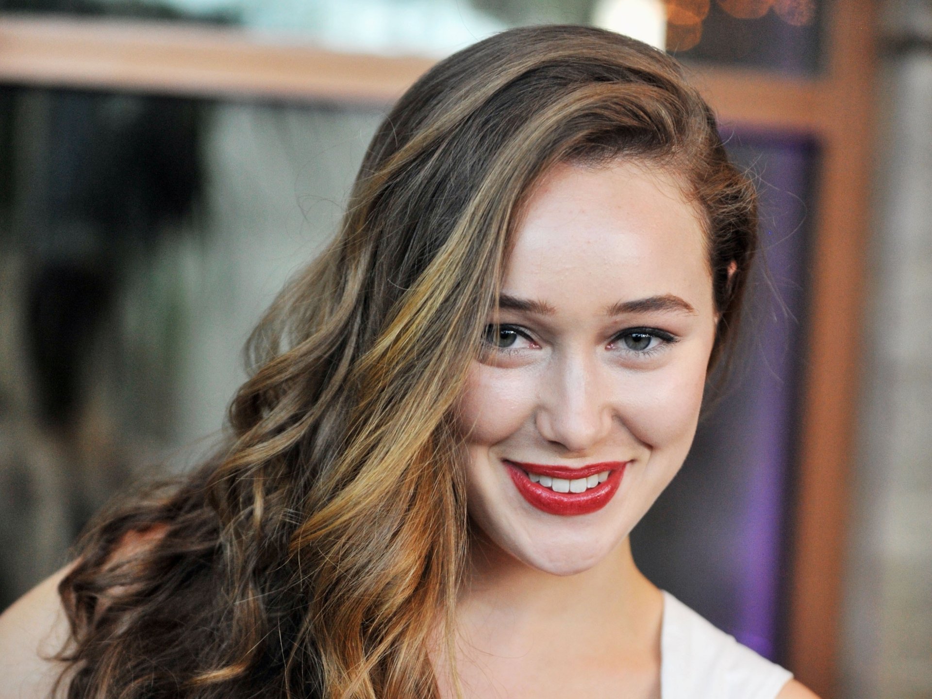 Close-up portrait of a smiling woman with long wavy hair and red lipstick, vivid 2K Quad HD PC desktop wallpaper and background.