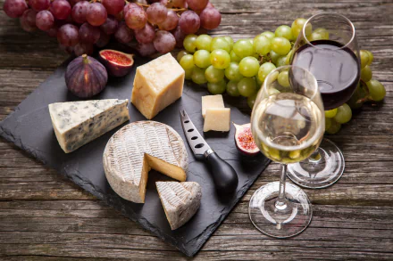 4K Ultra HD still life of wine glasses, assorted cheeses, figs, and green and red grapes arranged on a rustic wooden surface.