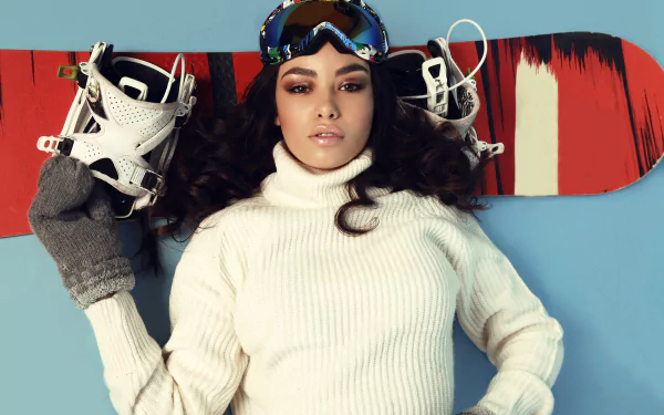 Brunette with brown eyes lies with a colorful snowboard behind her, wearing goggles and a white turtleneck — dynamic snowboarding sports 4K Ultra HD PC desktop wallpaper.