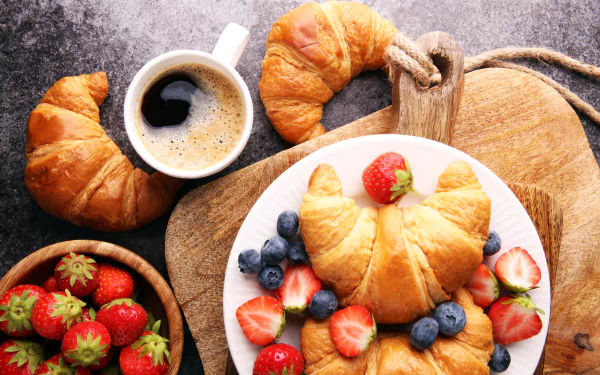 8K Ultra HD still life of a breakfast featuring croissants, fresh strawberries and blueberries, and a cup of coffee on a rustic wooden board.
