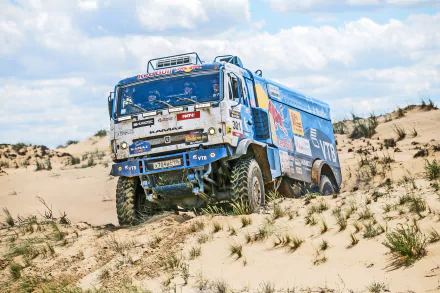 HD desktop wallpaper showing a Red Bull Kamaz rally vehicle tackling sand dunes in a desert, capturing the intensity of off-road sports rallying.