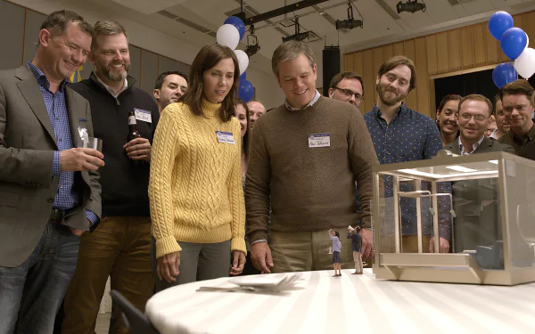 HD wallpaper featuring a scene from Downsizing with actors Matt Damon, Kristen Wiig, and others observing a small model house.