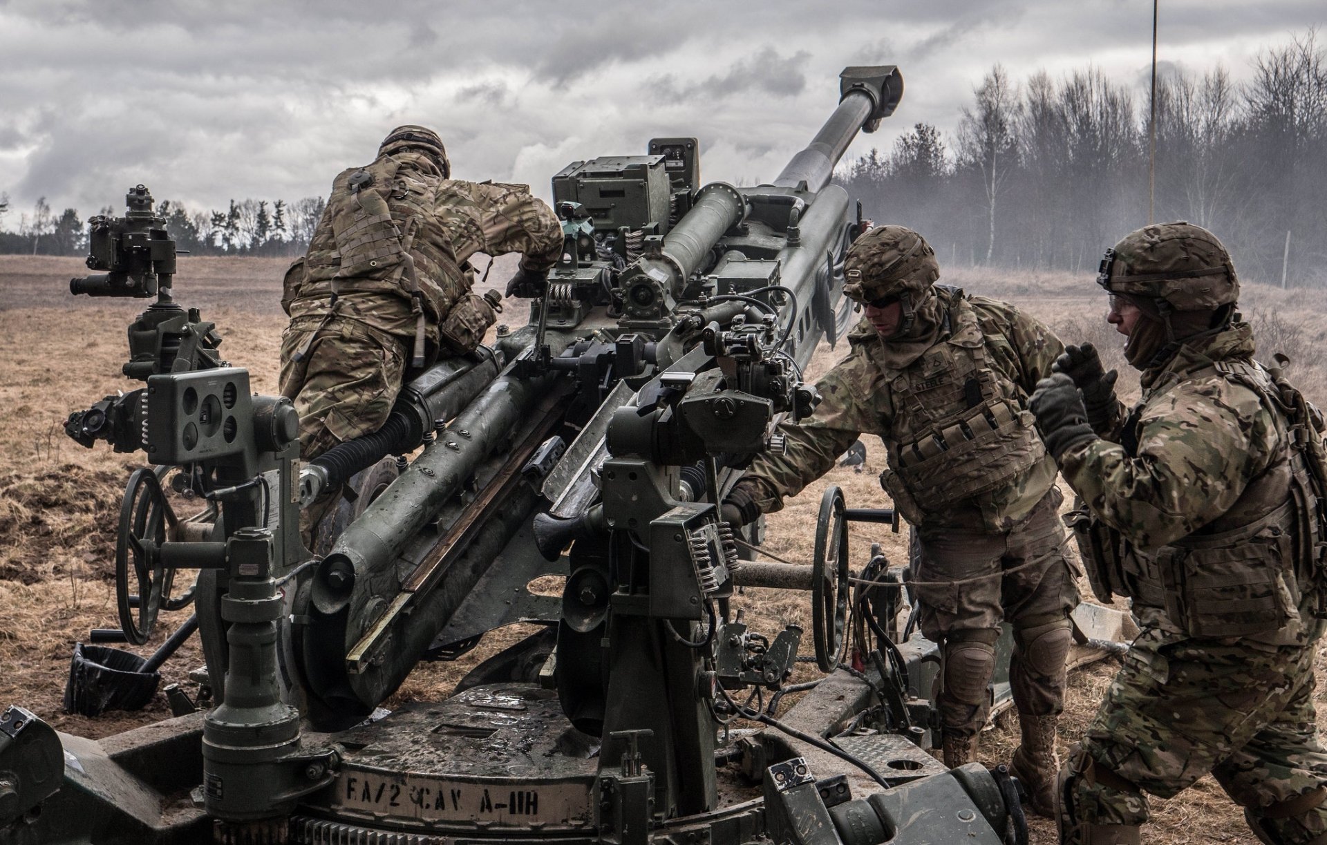 Soldiers operating heavy artillery in a military field, captured in a high-definition PC desktop wallpaper showcasing tactical readiness under a cloudy sky.