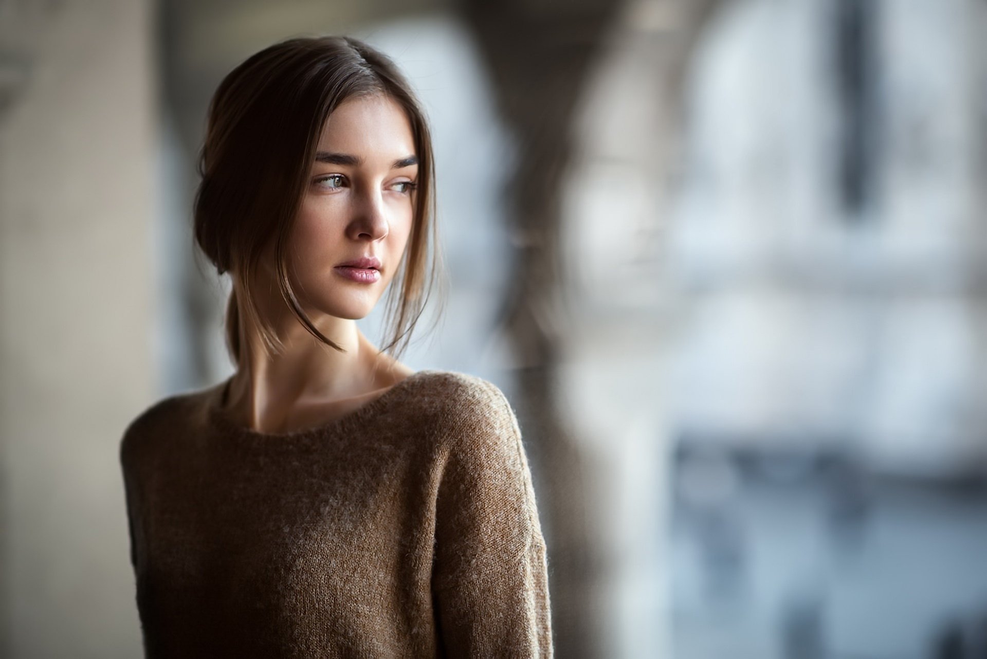 HD desktop wallpaper featuring a brunette woman model with a soft depth of field background, highlighting her contemplative expression and natural beauty.