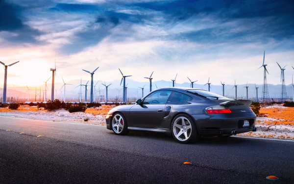 Silver Porsche 996 parked on a roadside at sunset with rows of wind turbines on the horizon — HD desktop wallpaper of a sleek car and wind farm under a dramatic sky