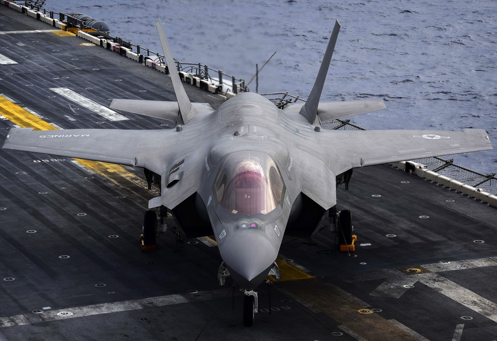 HD desktop wallpaper featuring a Lockheed Martin F-35 Lightning II jet fighter warplane on an aircraft carrier deck over the ocean.