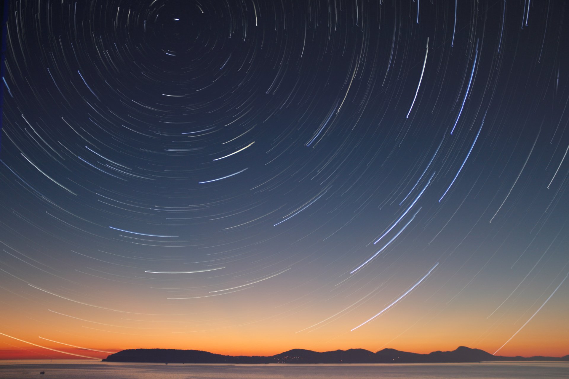 A 4K Ultra HD desktop wallpaper capturing stunning star trails over a dark night sky with a natural landscape silhouette at the horizon.