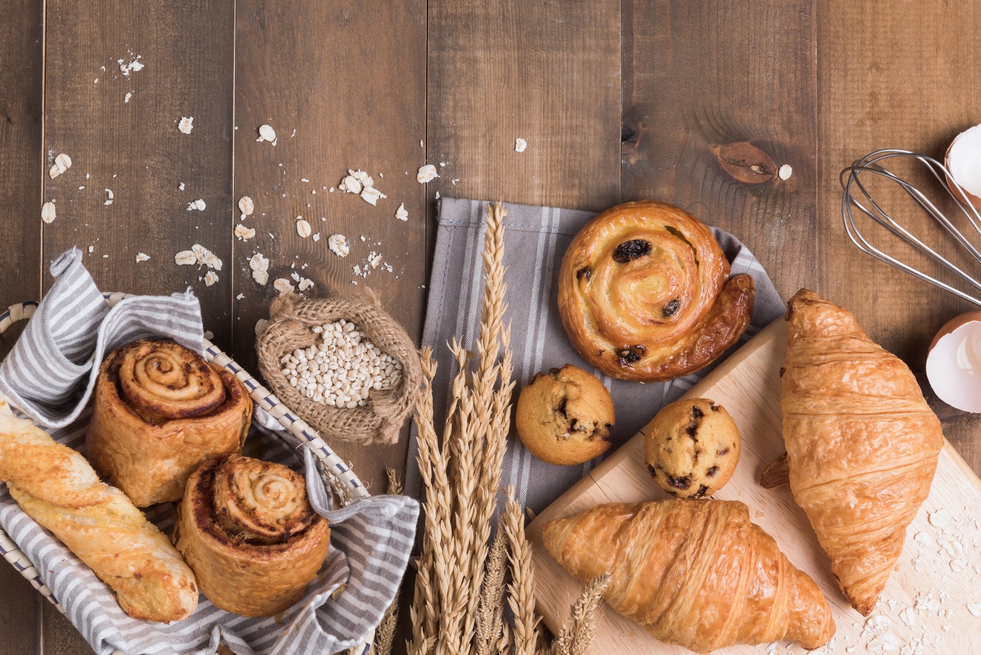 5K Ultra HD PC desktop wallpaper — still-life viennoiserie breakfast with croissants, pain aux raisins, cinnamon rolls and wheat on a rustic wooden table.