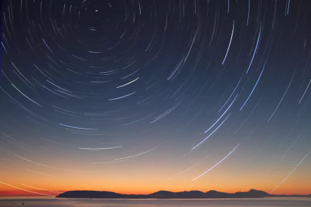A 4K Ultra HD desktop wallpaper capturing stunning star trails over a dark night sky with a natural landscape silhouette at the horizon.