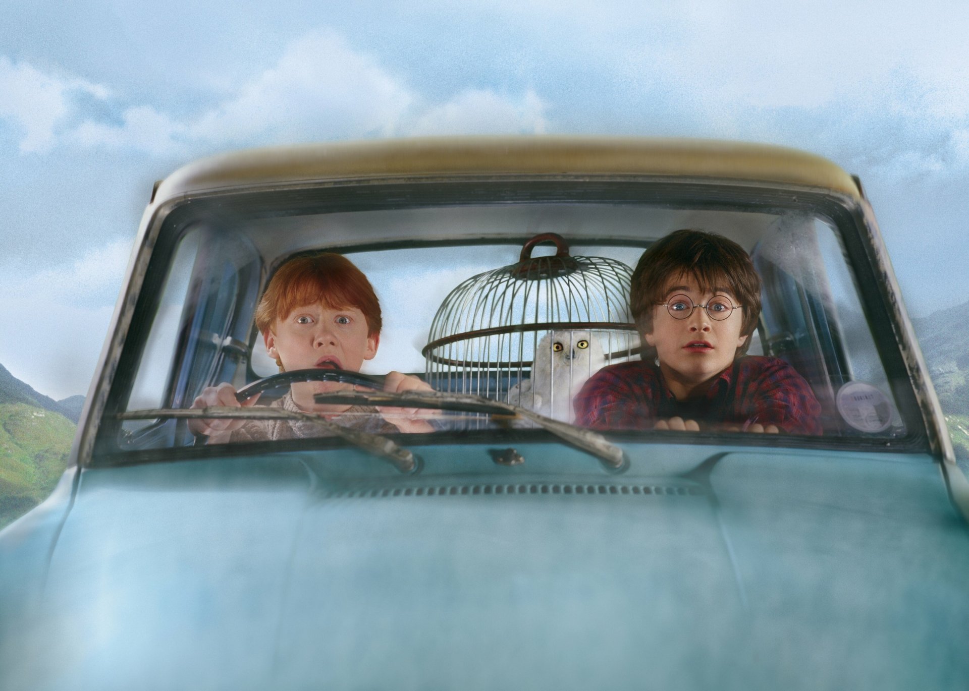 Rupert Grint as Ron Weasley and Daniel Radcliffe as Harry Potter are shown inside a car, with an owl in a cage, from Harry Potter and the Chamber of Secrets. HD desktop wallpaper.