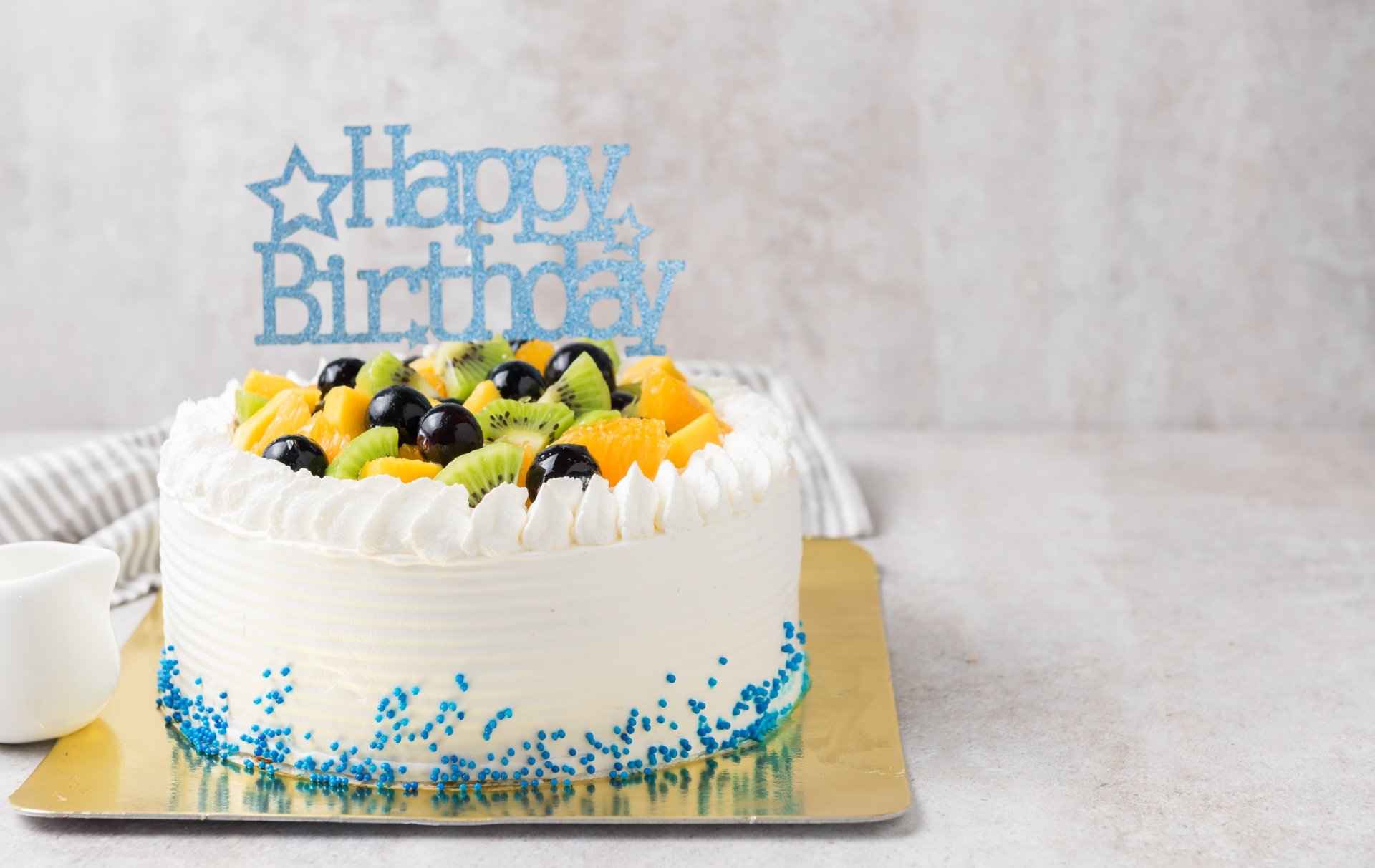 A vibrant pastry cake topped with assorted fresh fruits and a blue Happy Birthday topper, captured as a 4K Ultra HD holiday birthday wallpaper.
