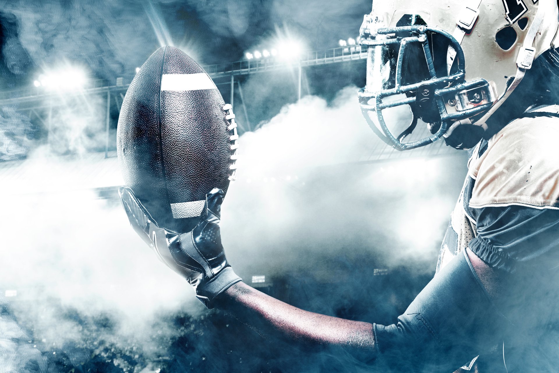 4K Ultra HD desktop wallpaper featuring a close-up of an American football player holding a football, surrounded by dramatic smoke and stadium lights, capturing intense sports action.