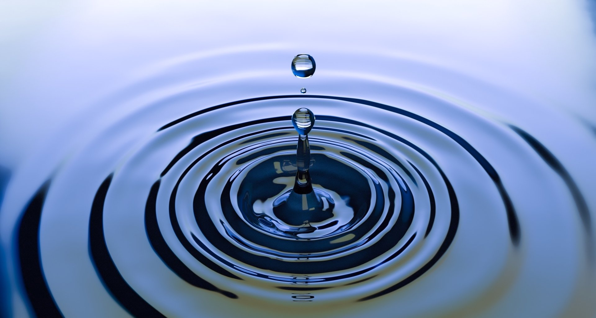 2K Quad HD PC desktop wallpaper showing close-up water photography: a single droplet splashing into concentric ripples.