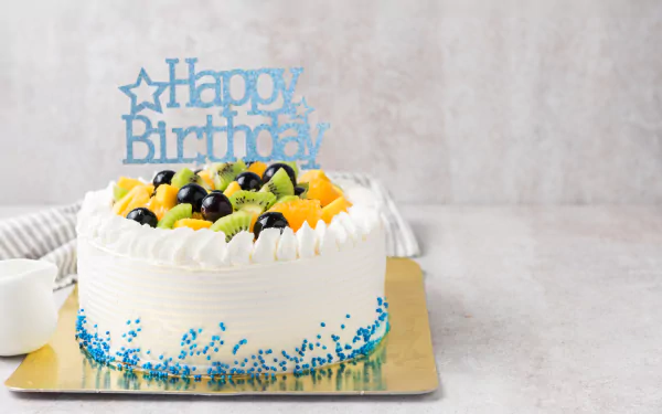 A vibrant pastry cake topped with assorted fresh fruits and a blue Happy Birthday topper, captured as a 4K Ultra HD holiday birthday wallpaper.