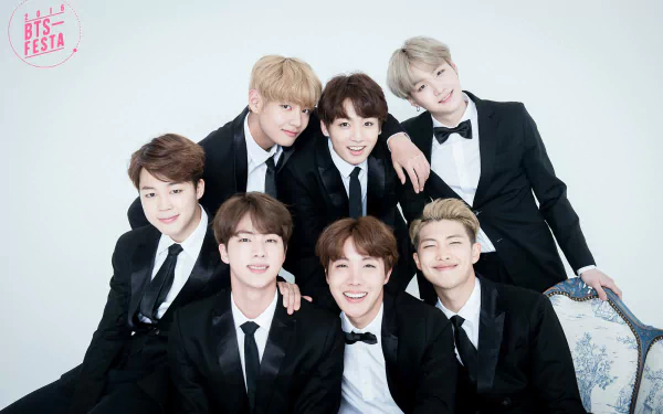 HD desktop wallpaper featuring the music group BTS dressed in formal black suits, smiling and posing together against a clean, white background.
