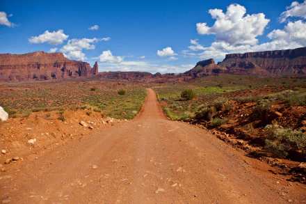 4K Ultra HD landscape wallpaper featuring a dirt road stretching through a desert with rocky formations under a bright blue sky with scattered clouds.