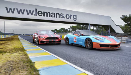 4K Ultra HD desktop wallpaper of a red Ford Mustang GT and blue-orange Chevrolet Corvette (C6) sports cars side-by-side on the Le Mans racetrack.