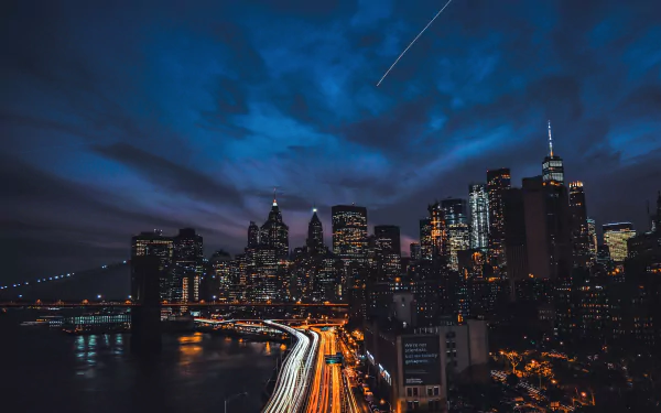 Time-lapse 4K Ultra HD wallpaper of New York City skyline at night, featuring illuminated skyscrapers, a glowing bridge, and a meteor streaking across the sky.