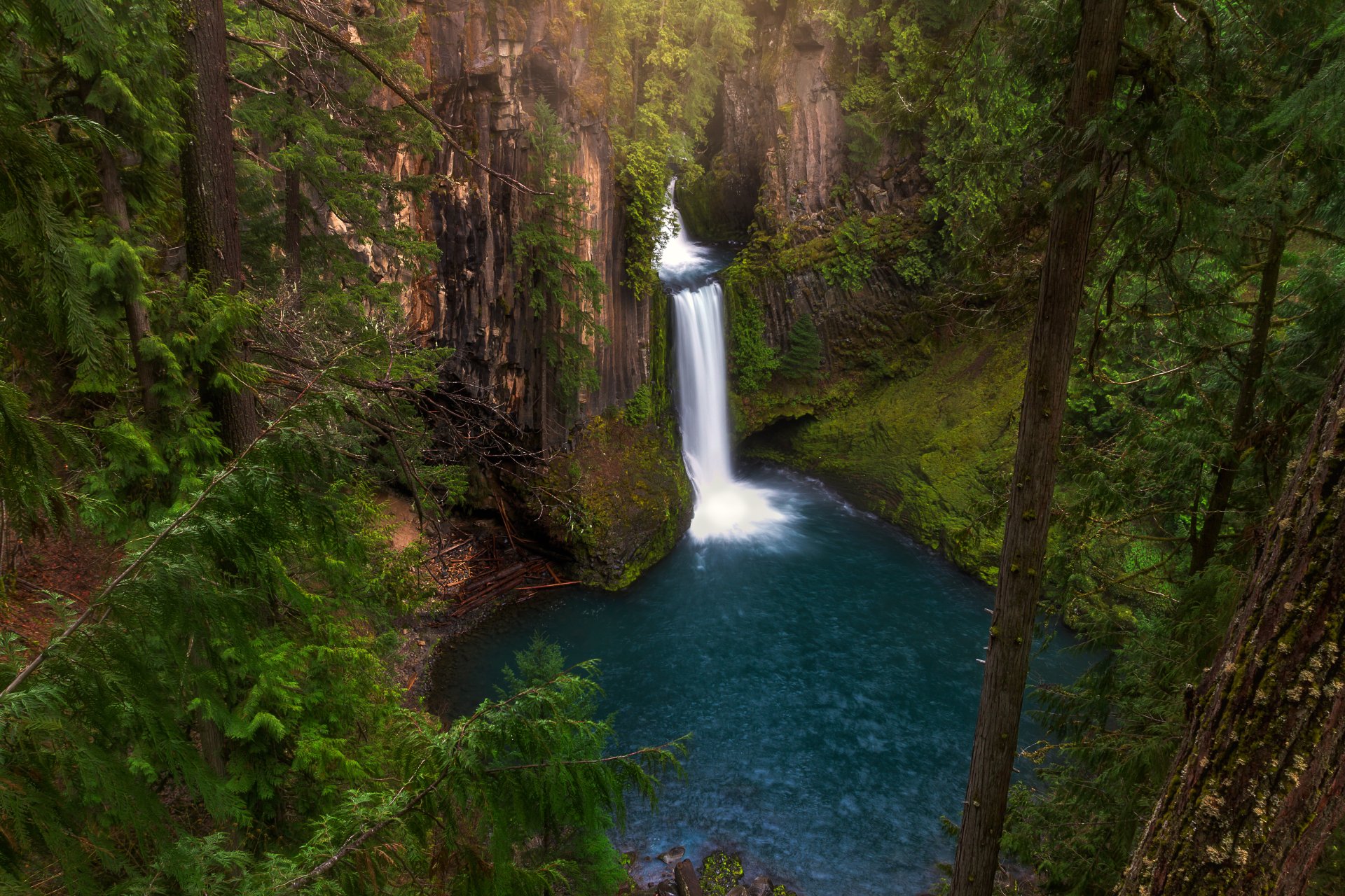 A stunning HD desktop wallpaper of a serene lake nestled among lush greenery, featuring a mesmerizing waterfall cascading down a cliff.