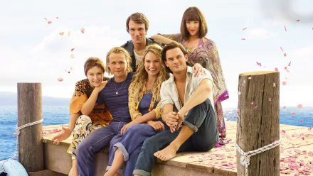 4K Ultra HD PC desktop wallpaper featuring the cast of the movie Mamma Mia! Here We Go Again, sitting together on a dock surrounded by water and petals.