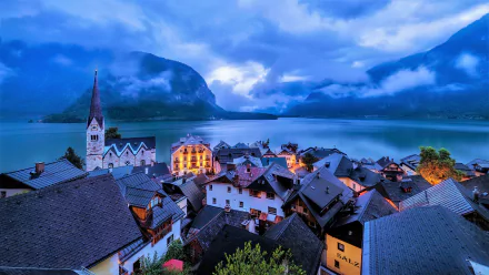 A winter evening view of Hallstatt, Austria, showcasing snow-dusted mountain peaks, a serene lake, and the town's charming architecture under a moody sky in 4K Ultra HD.