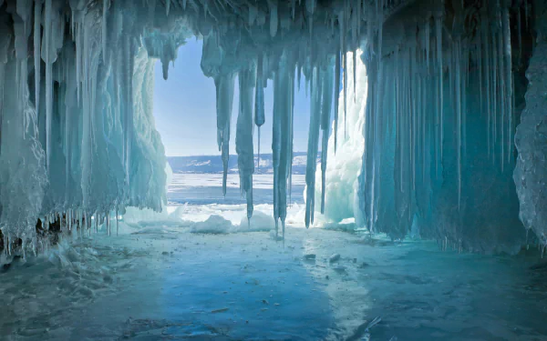 8K Ultra HD winter cave scene showcasing nature’s icy stalactites and frozen floor, framing a bright, cold landscape beyond the ice formations.