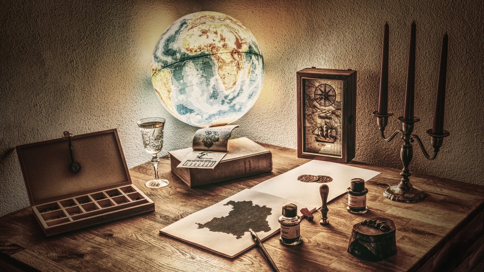 Vintage still life featuring a globe, compass, candle holder with candles, old books, and map pieces on a wooden desk, captured in HD for a desktop wallpaper background.