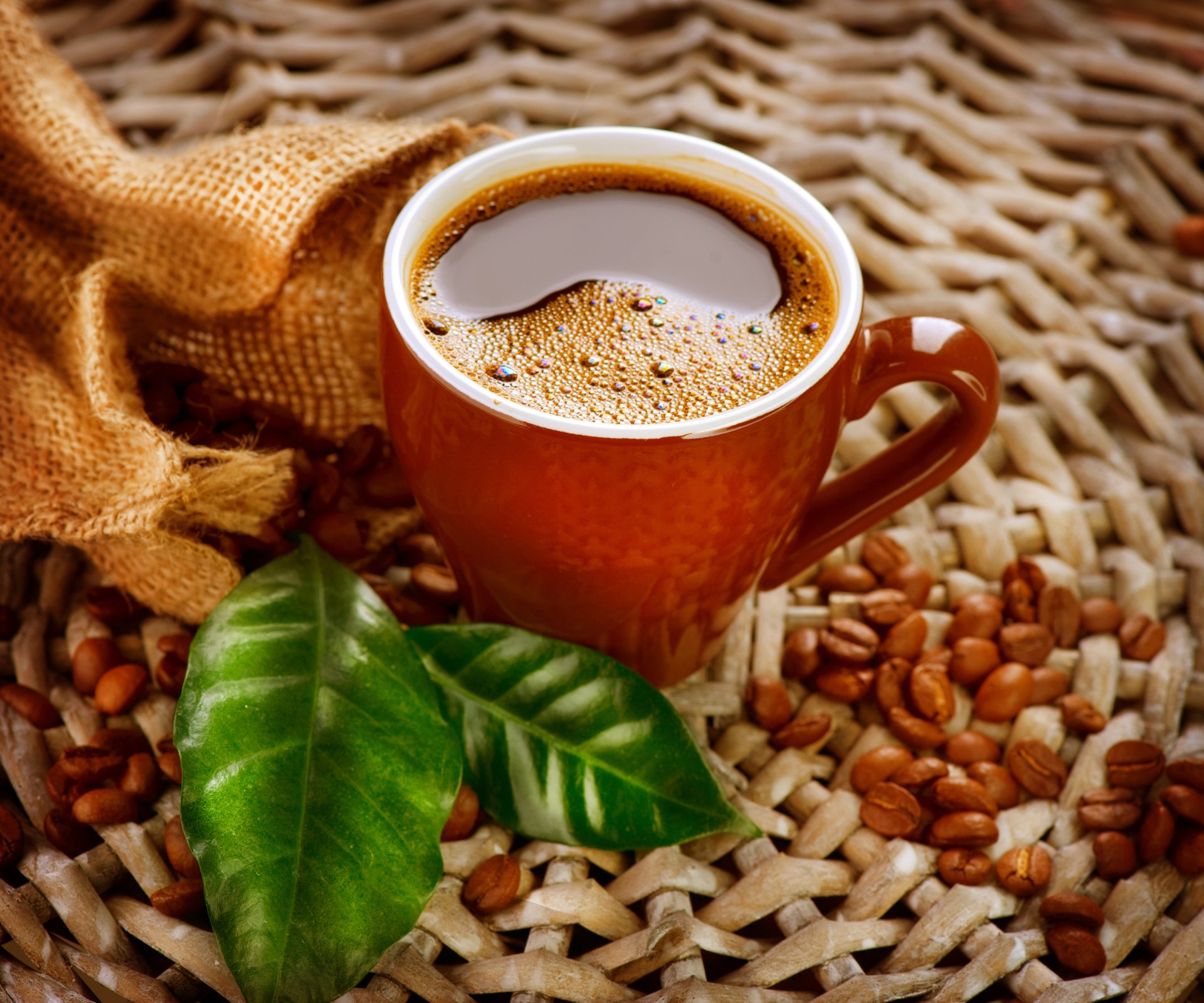 2K Quad HD PC desktop wallpaper/background: still-life of a steaming coffee cup with roasted coffee beans and green leaves on a woven mat.