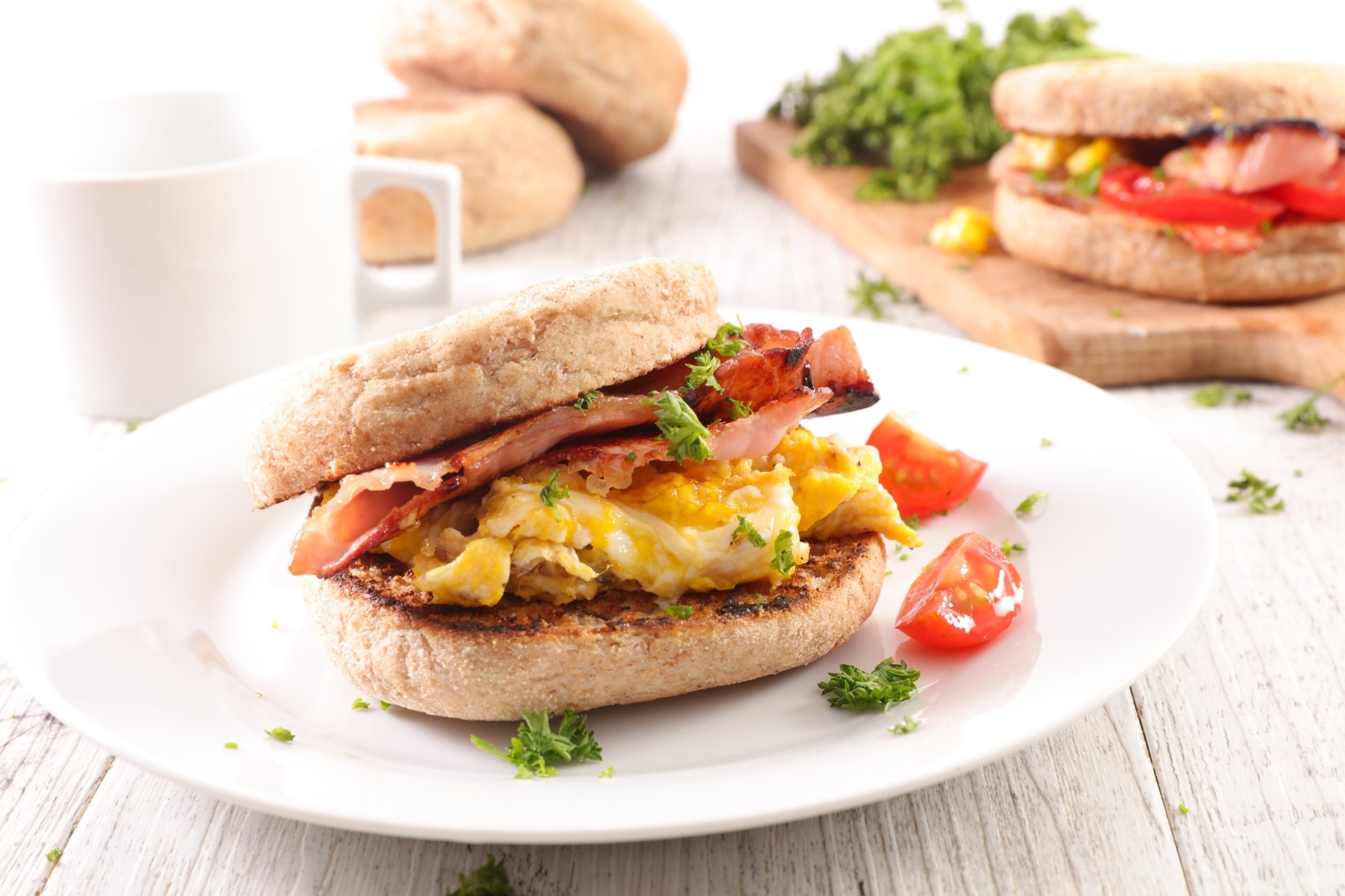 8K Ultra HD still life of a breakfast sandwich with eggs, bacon, and tomatoes on a white plate, set against a bright background with fresh ingredients.