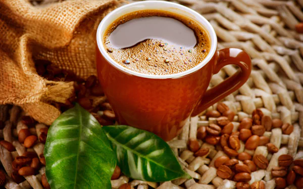 2K Quad HD PC desktop wallpaper/background: still-life of a steaming coffee cup with roasted coffee beans and green leaves on a woven mat.