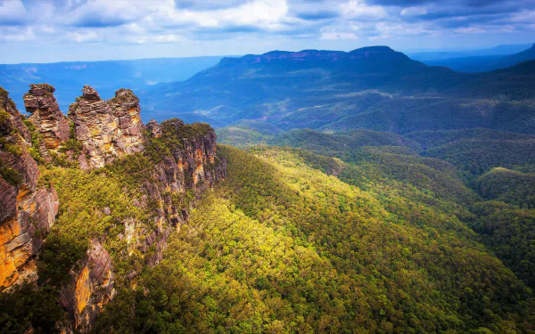 A panoramic view of the stunning Blue Mountains landscape in Katoomba, Australia, showcasing the iconic Three Sisters rock formation against a lush forest backdrop. 